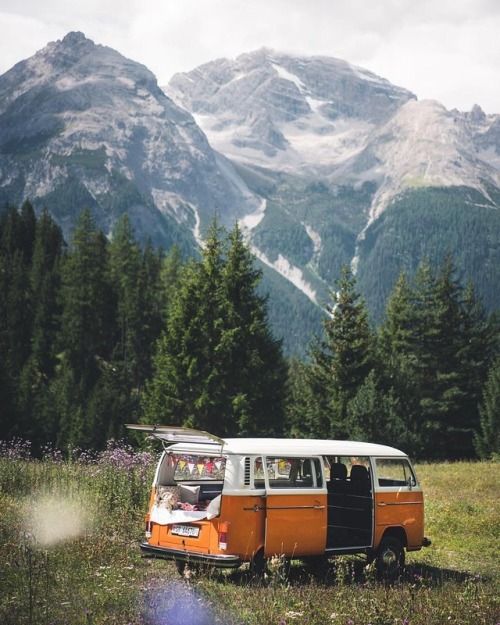 an orange and white van parked on top of a grass covered field next to mountains