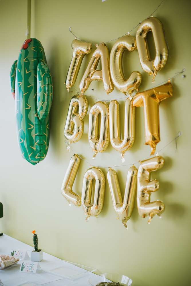 balloons that spell out the word taco bout love are hanging on a wall above a table