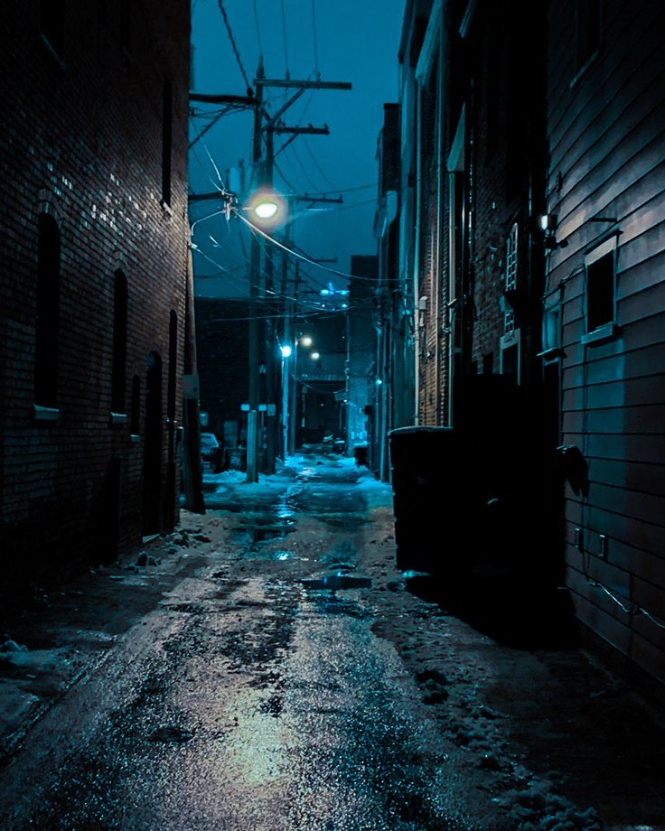 a dark alley way with snow on the ground and street lights in the distance at night