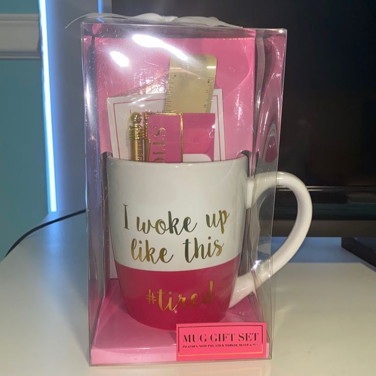 a pink and white coffee mug with writing on it in a clear plastic box next to a computer monitor