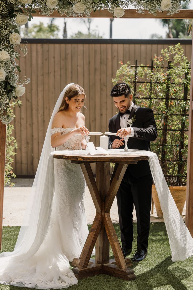 the bride and groom are signing their marriage vows under an arch decorated with white flowers