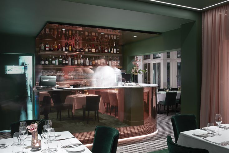 the interior of a restaurant with green walls and white tablecloths, chairs, and bar