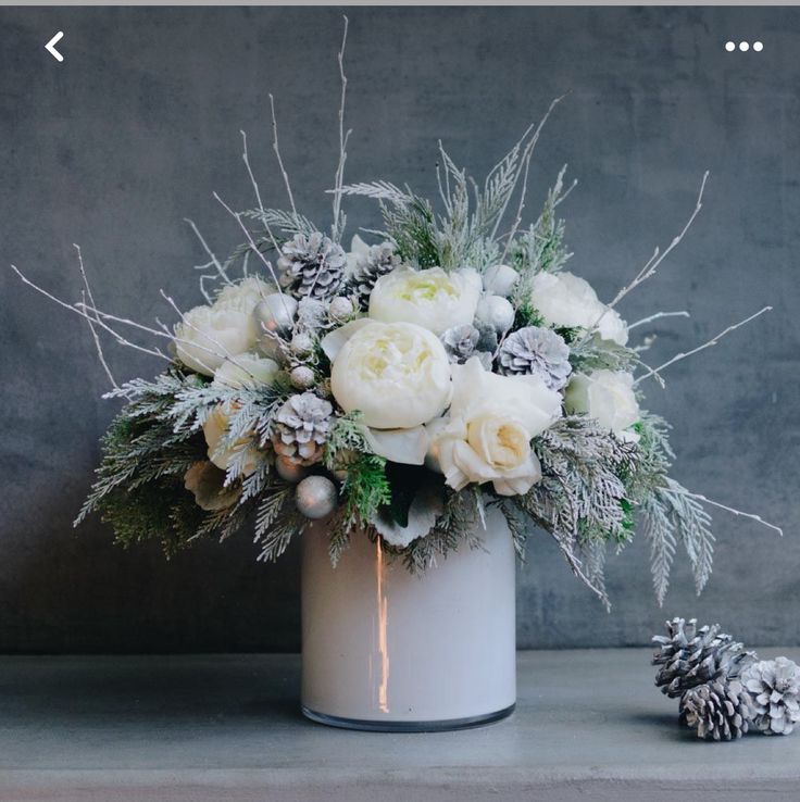 a white vase filled with flowers next to pine cones and snow flakes on top of a table