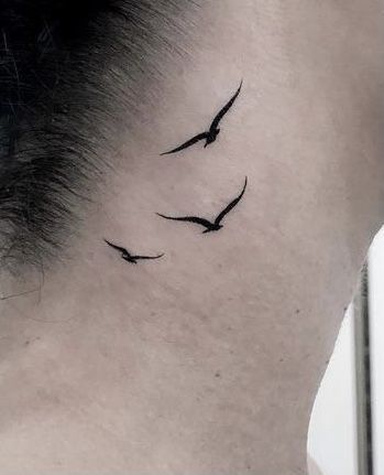 a woman's neck with two birds tattoo on the back of her left shoulder