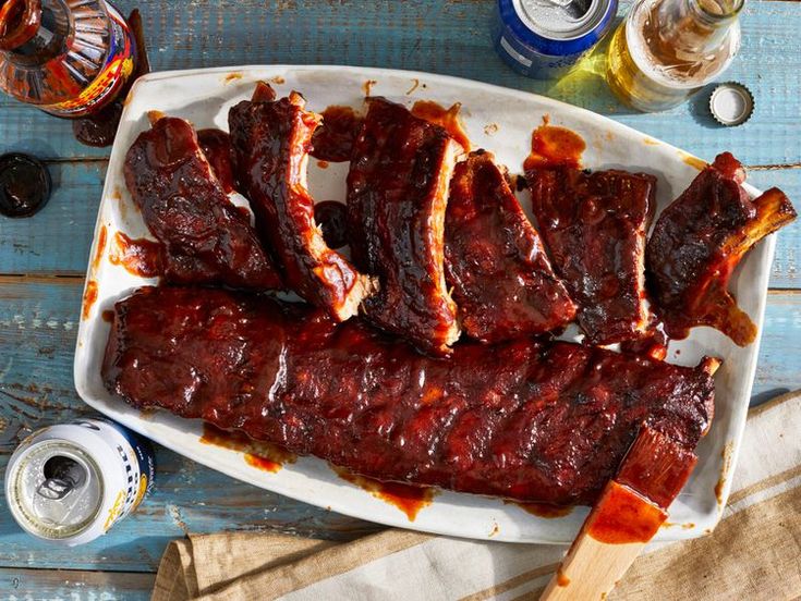 ribs covered in bbq sauce on a white platter next to beer bottles and napkins