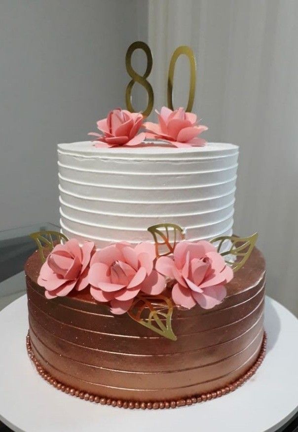 a three tiered cake with pink flowers on top and the number 80 written in gold