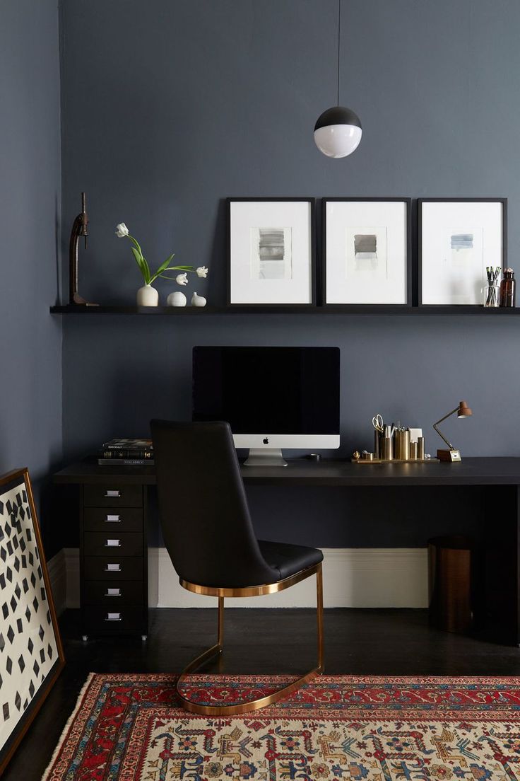 a desk with a computer on top of it in front of two framed pictures and a rug