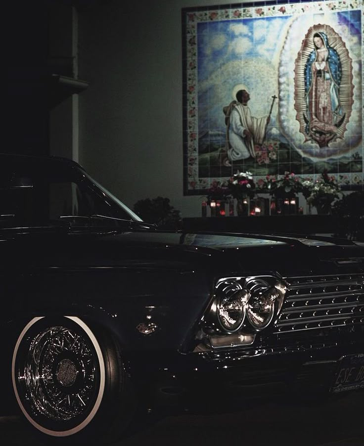 an old black car parked in front of a painting