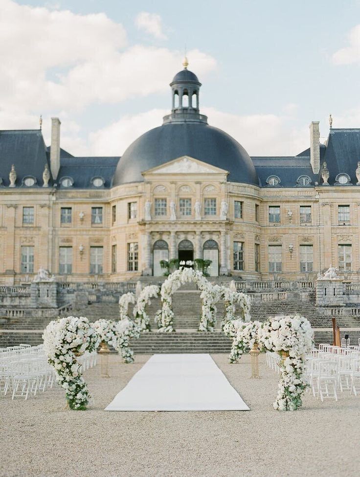 an outdoor wedding setup with white flowers and greenery in front of a large building