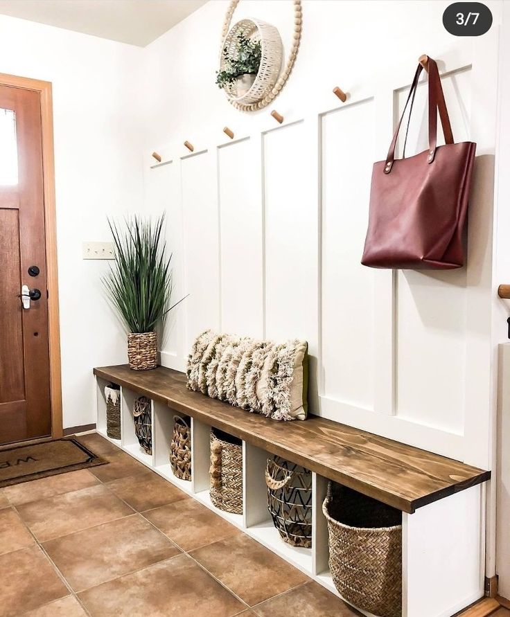 a wooden bench sitting next to a white wall with baskets on it and a purse hanging from the back