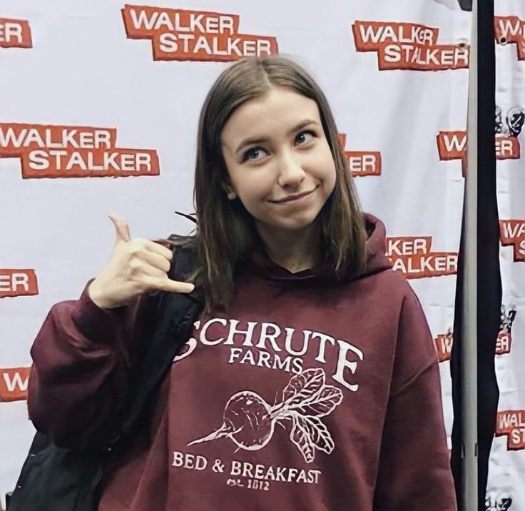 a girl in a maroon hoodie points at the camera