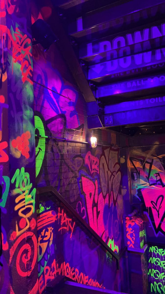 colorful graffiti painted on the walls and stairs in an underground area with purple light coming from above