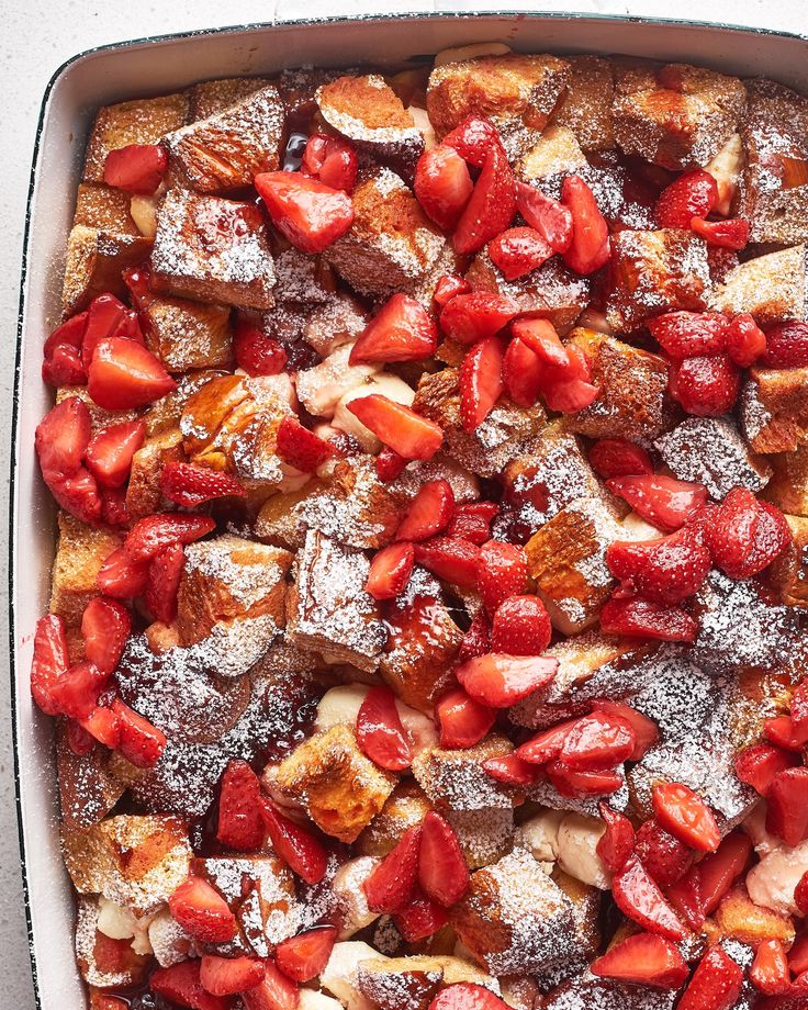 a pan filled with french toast and strawberries covered in powdered sugar