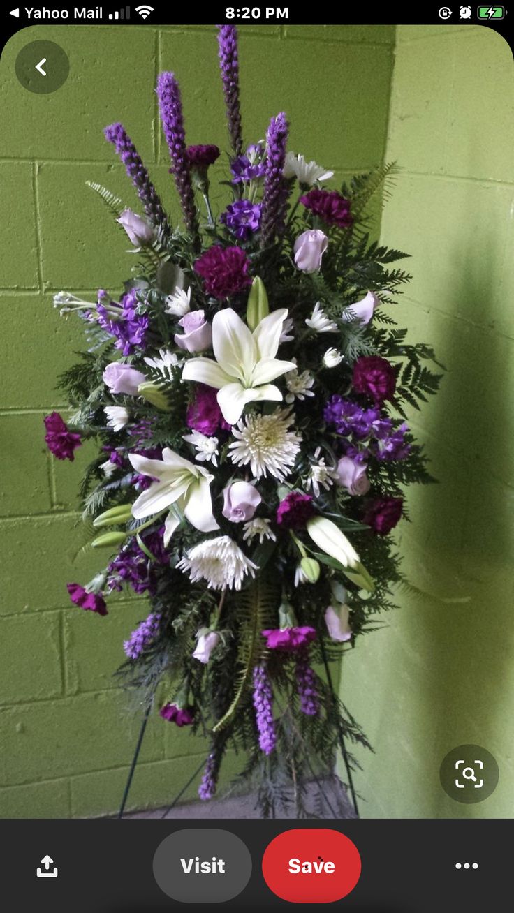 a purple and white flower arrangement in front of a green wall