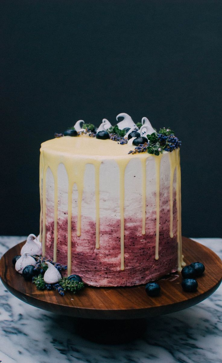 a cake with white icing and blueberries on a wooden platter next to a black wall