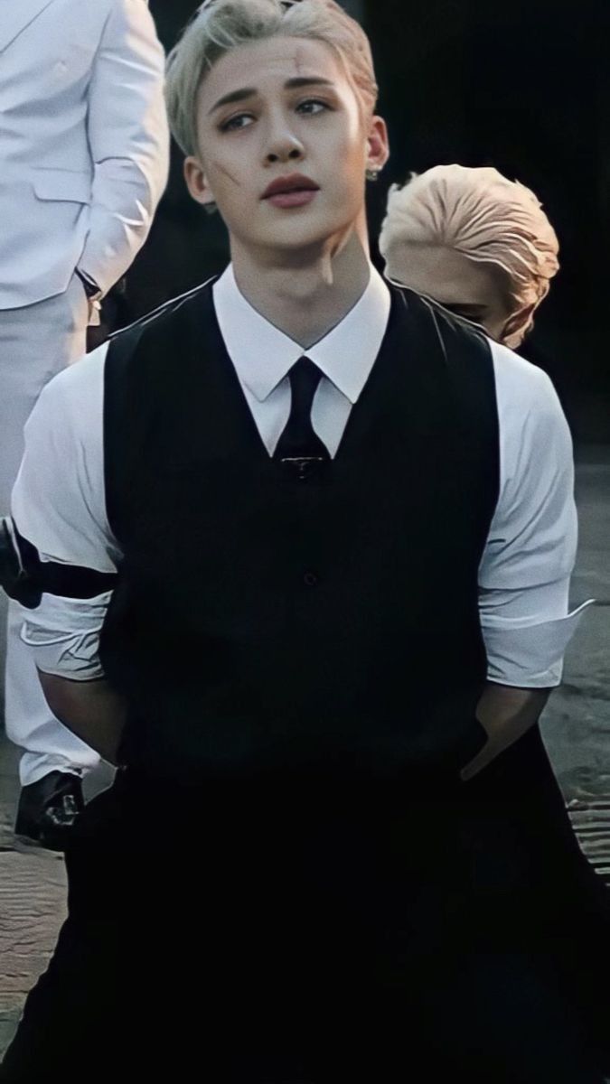 a man in a black vest and tie sitting on the ground with other people behind him