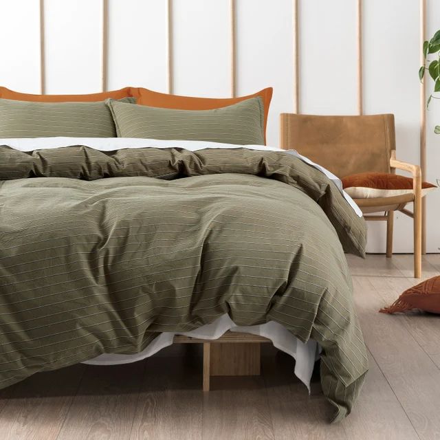 a bed with green sheets and pillows in a white room next to a wooden chair