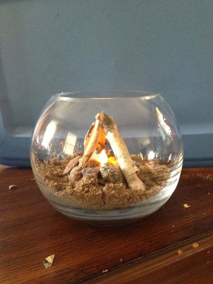 a glass bowl filled with sand and some kind of fire in it on top of a wooden table