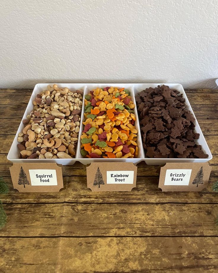 three trays filled with different types of food on top of a wooden table in front of a white wall