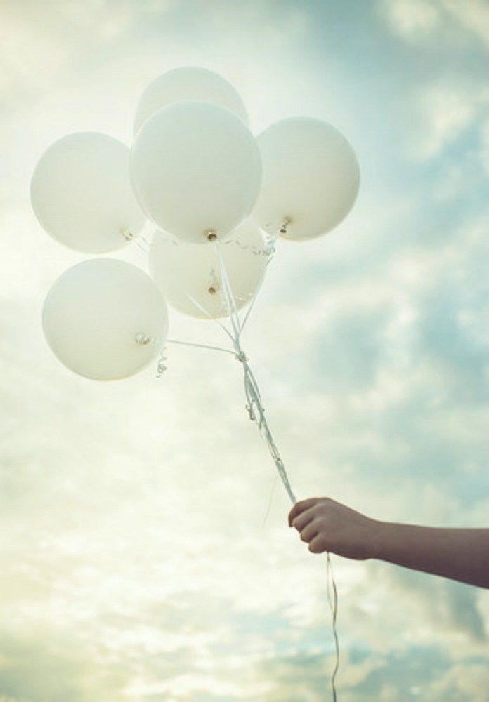 a person holding several white balloons in the air with sky and clouds behind them at sunset