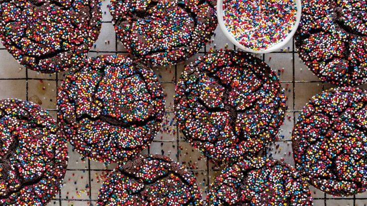 sprinkle covered donuts sitting on top of a cooling rack next to a spoon