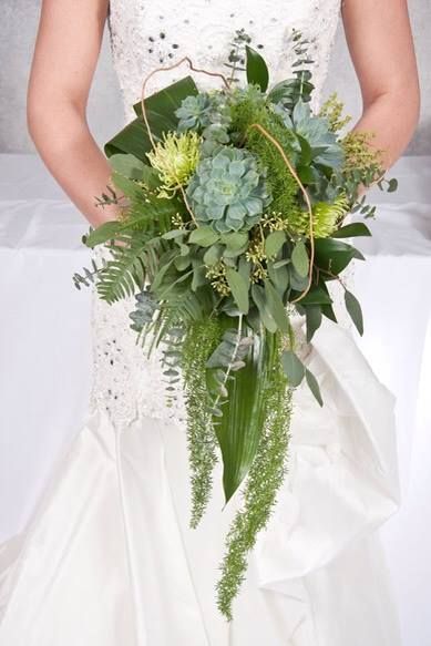 a woman in a wedding dress holding a bouquet with greenery and succulents