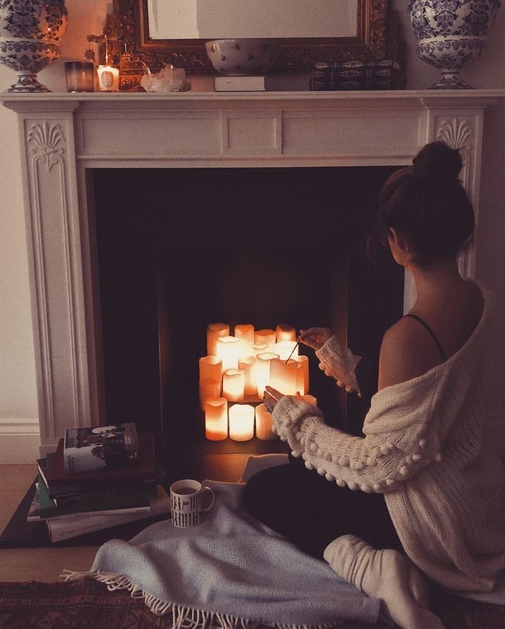 a woman sitting on the floor next to a fireplace with candles in front of her