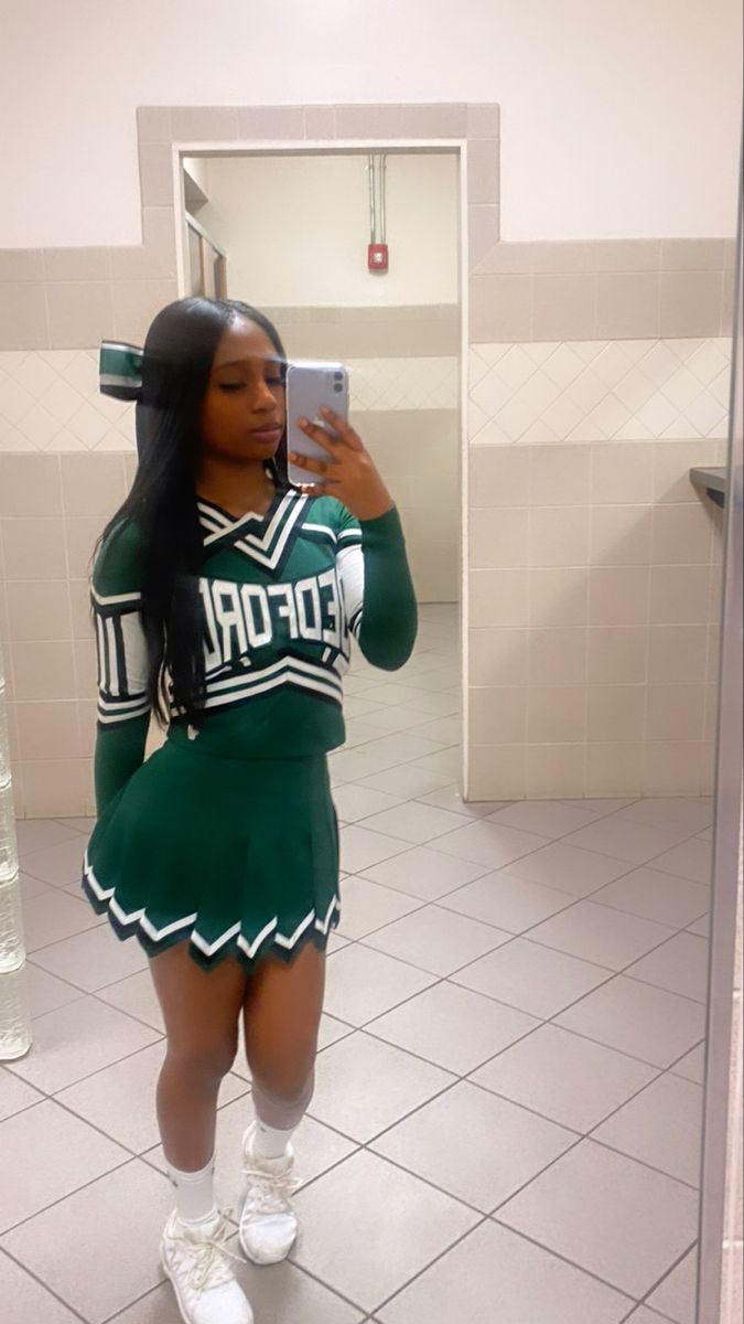 a woman taking a selfie in a bathroom mirror wearing a cheerleader outfit and holding a cell phone