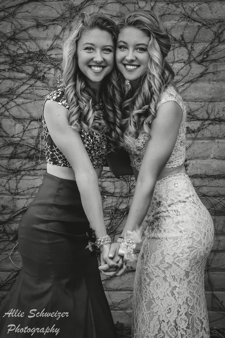 two beautiful young women standing next to each other in front of a brick wall holding hands