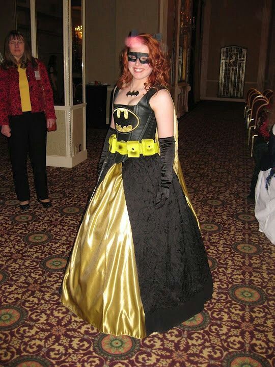 a woman in a batman costume standing on a carpeted floor with other people behind her