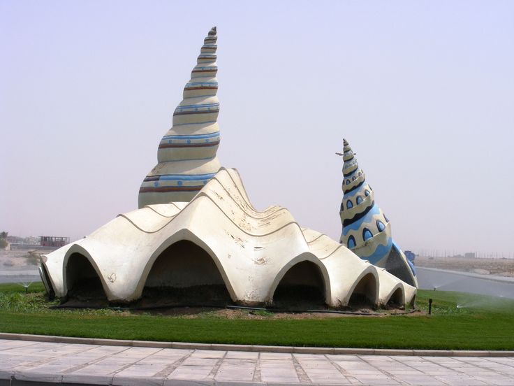 an artisticly designed building sits in the middle of a grassy area next to a paved road