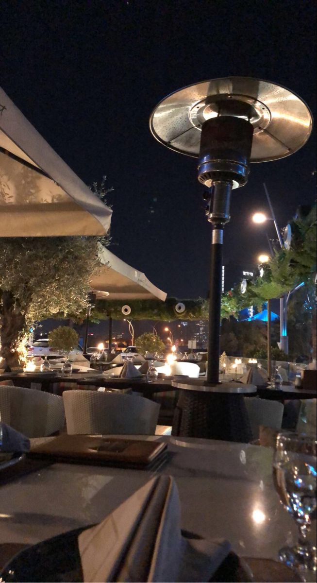 an outdoor dining area at night with tables and umbrellas over looking the street lights