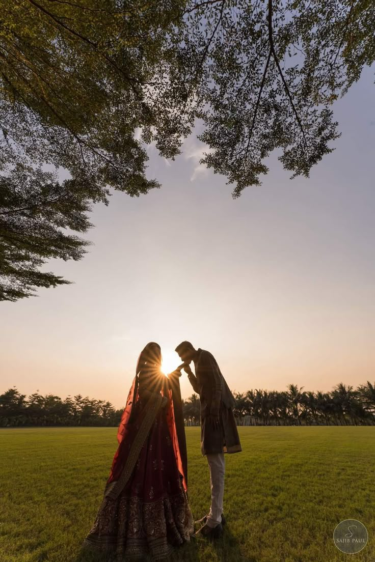 two people standing in the grass near each other, facing each other as the sun sets behind them