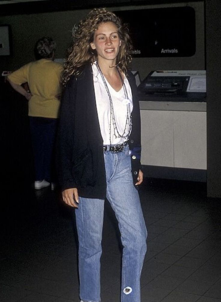 a woman standing in an airport wearing jeans and a white t - shirt is smiling at the camera