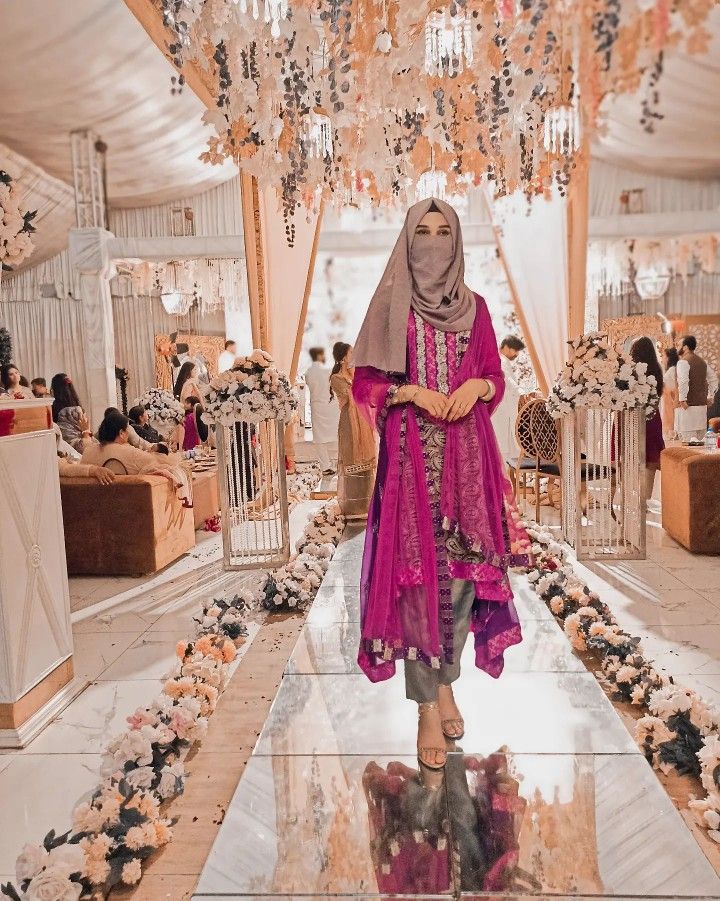 a woman wearing a hijab standing in a room filled with flowers and chandeliers