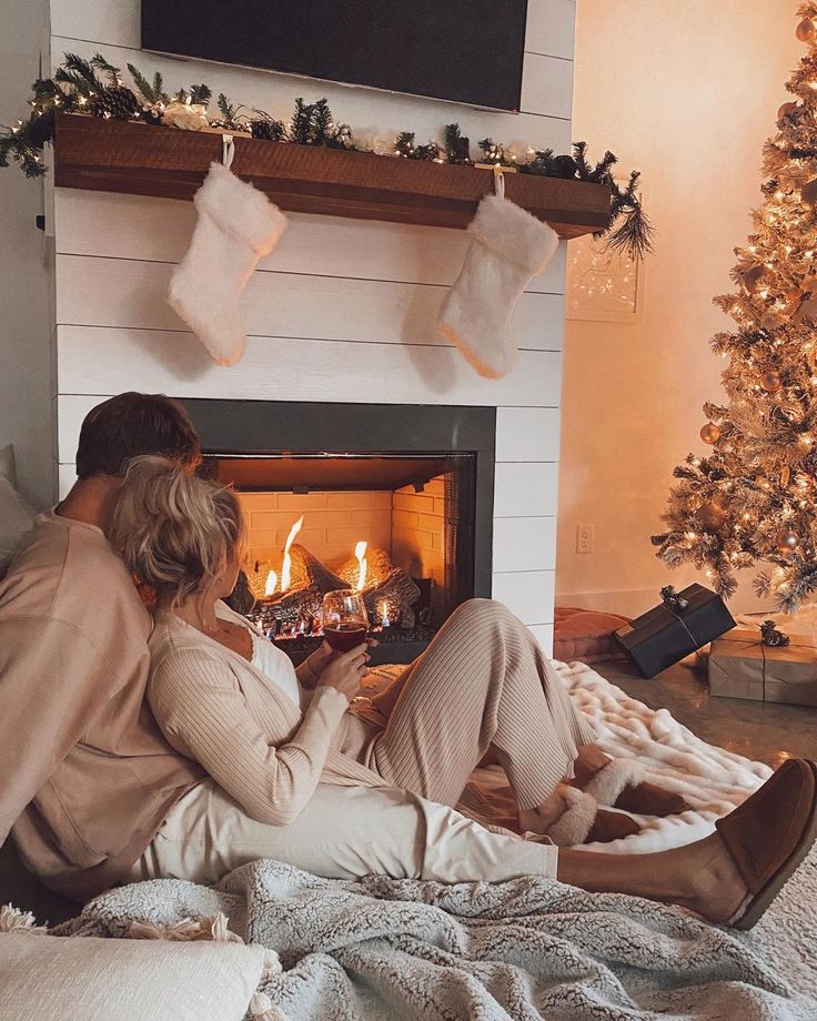 a man and woman sitting in front of a fireplace with stockings hanging over the fire