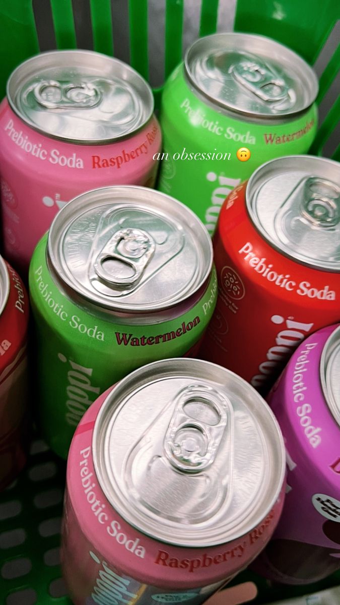 many cans of soda are stacked in a green basket and one is pink, red, yellow, purple, and green