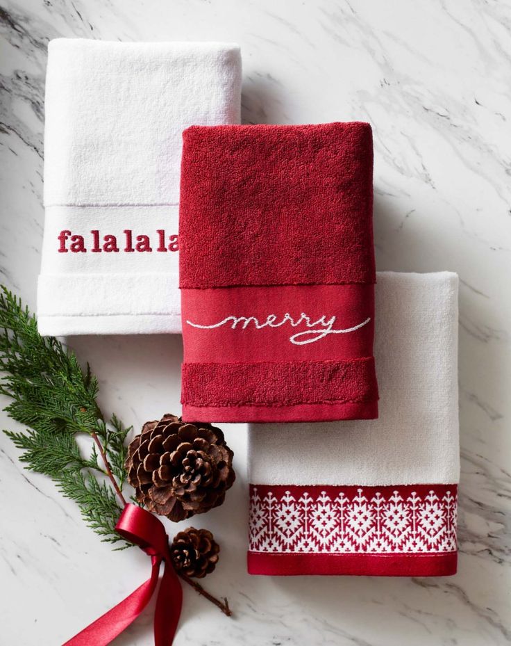 three red towels with merry written on them next to pine cones and a ribbon tied around the edges