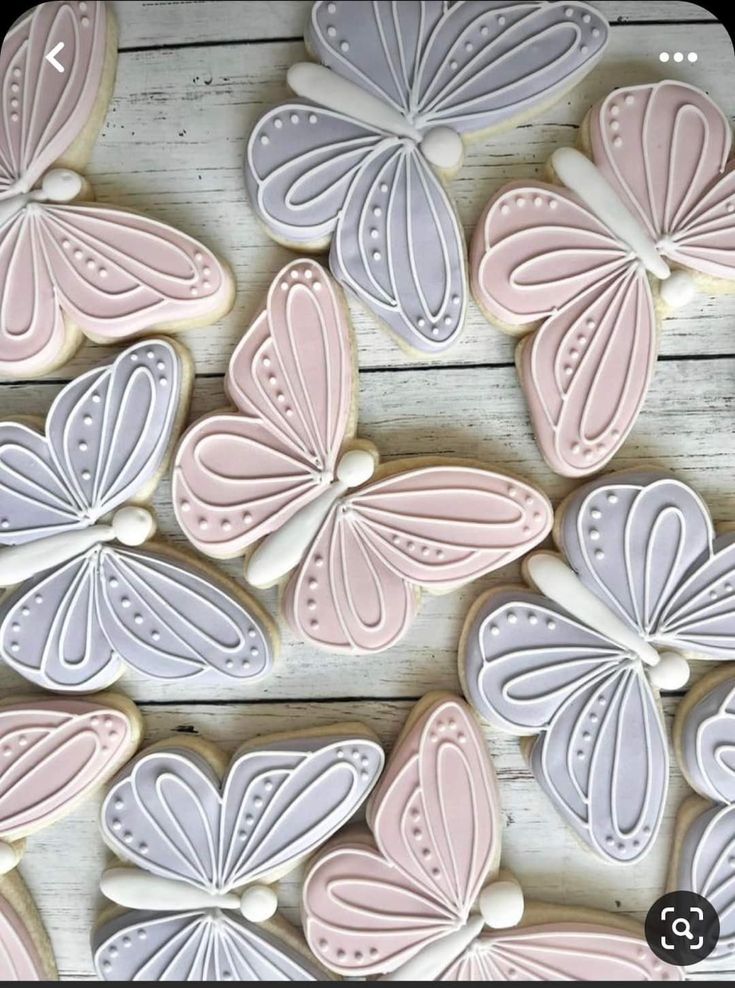 decorated cookies with pink and white butterflies on top of a wooden table in the shape of butterfly wings