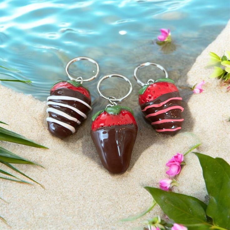 three chocolate covered strawberries sitting on top of sand next to a body of water