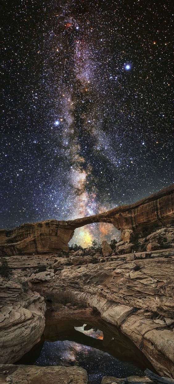 the night sky with stars above rocks and an arch in the foreground, as seen from below