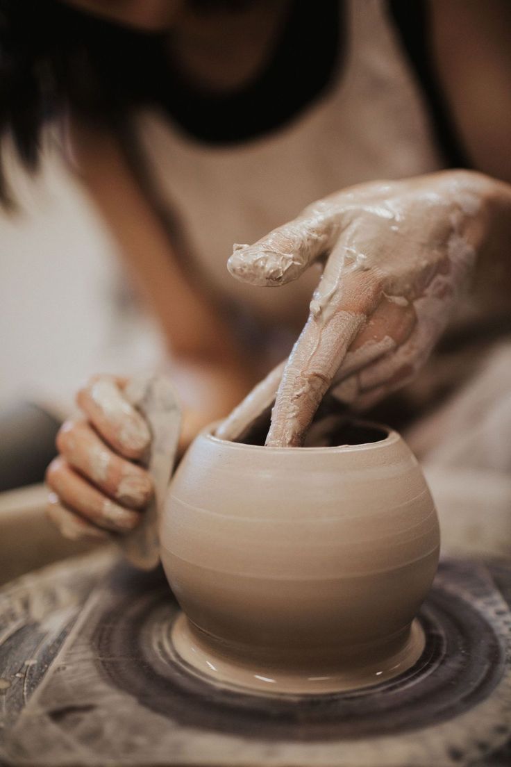 a woman is making a vase on a potter's wheel with her hands in it