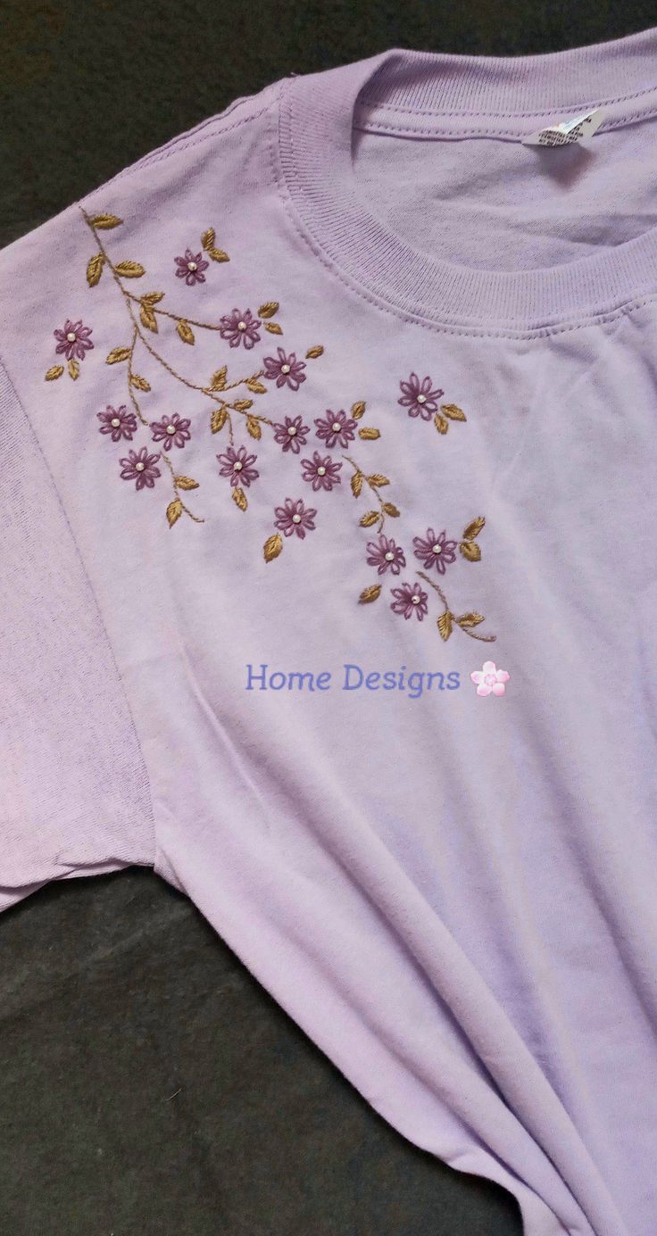 a t - shirt with embroidered flowers on it sitting on the floor next to a pair of scissors