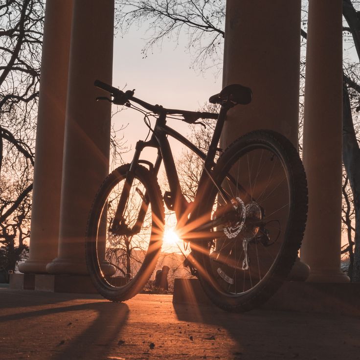 a bike is parked in front of some pillars with the sun shining through it's windows