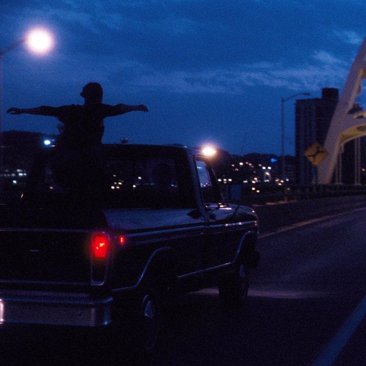 a man standing on the back of a pickup truck in front of a bridge at night