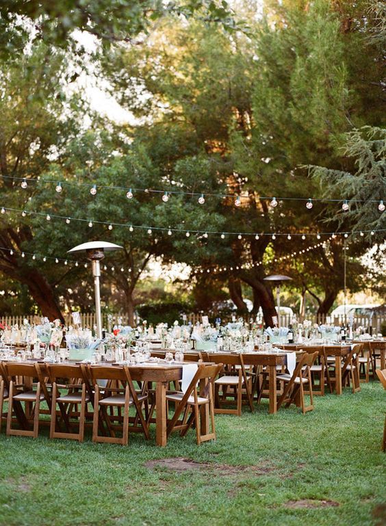 an outdoor dining area with wooden chairs and tables set up for a wedding reception in the woods