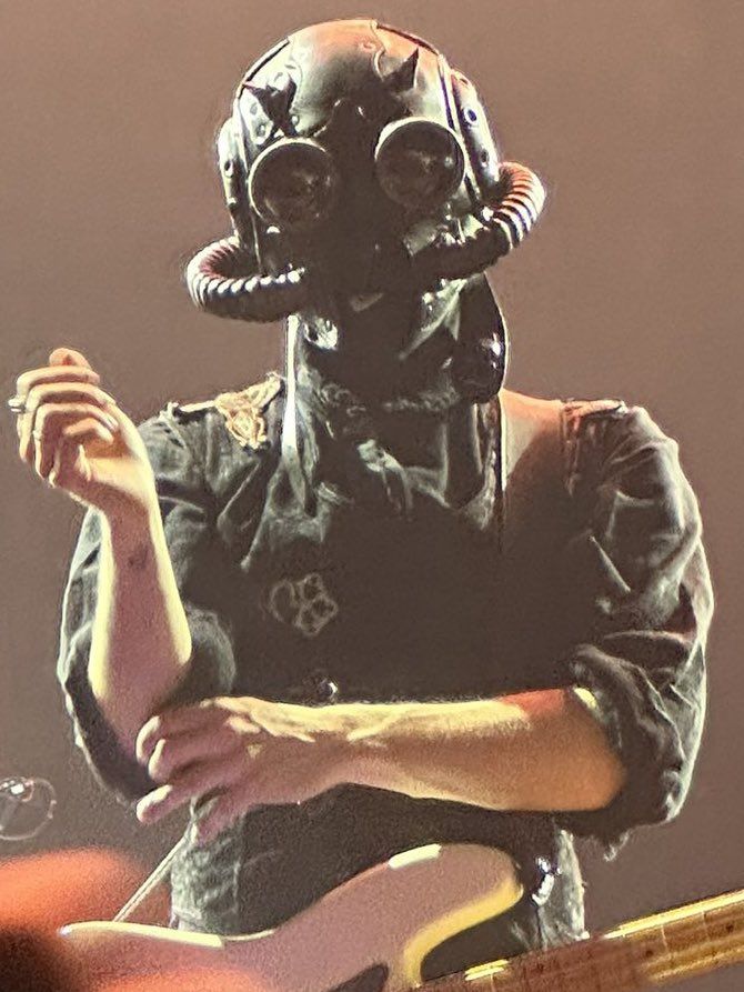 a man wearing a mask and holding a guitar in front of him with his hands