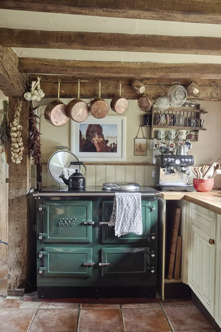 an old fashioned green stove in a kitchen with pots and pans hanging on the wall