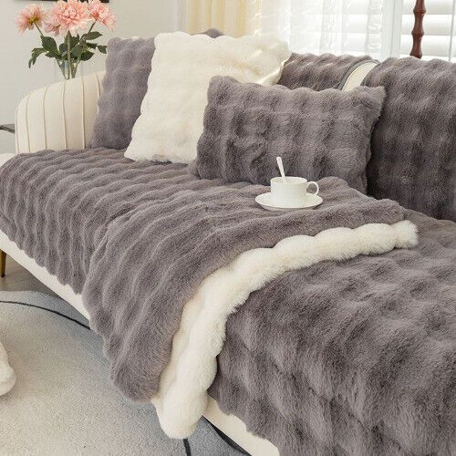 a couch covered in grey and white fur with a cup on the arm rest next to it