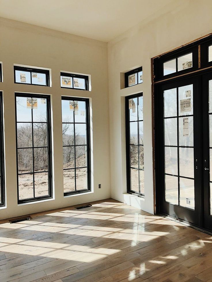 an empty room with three large windows and wood flooring on the side of it